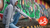 Young man wearing a hoodie and sat in front of a graffiti wall